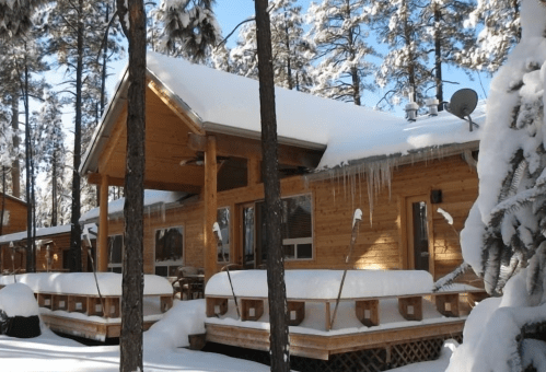 A cozy wooden cabin surrounded by snow-covered trees, with icicles hanging from the roof.